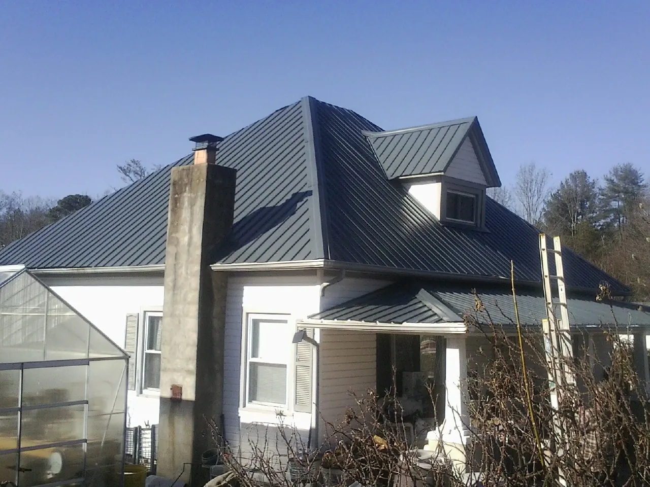 Dark blue standing seam metal roof on a white farmhouse with dormer — Slate & Tile Roof Repair by Roofing Brothers in Newton Grove