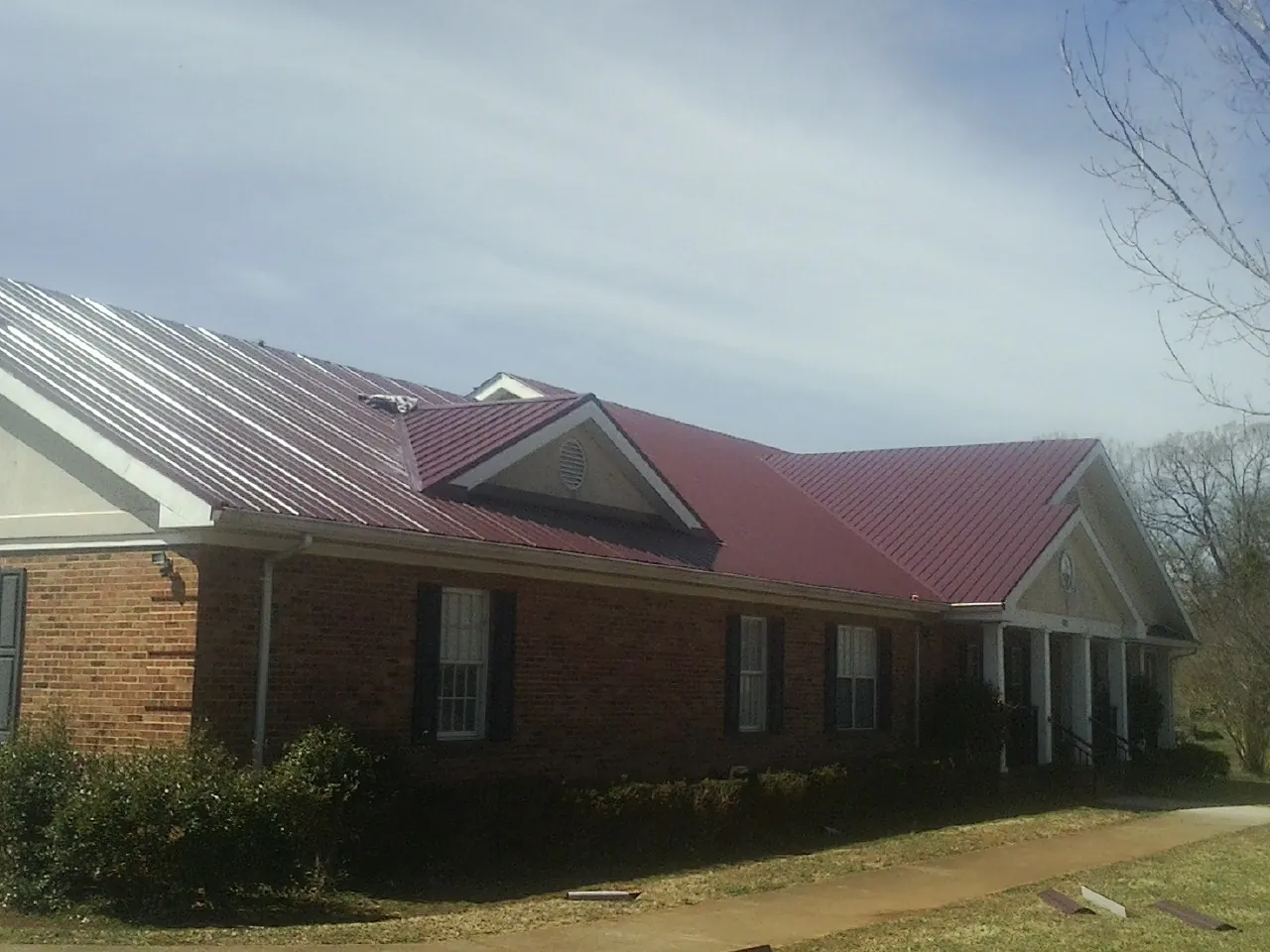 Red metal roof with gabled entries on a long brick building, from a Hail Damage Roof Repair job in Newton Grove