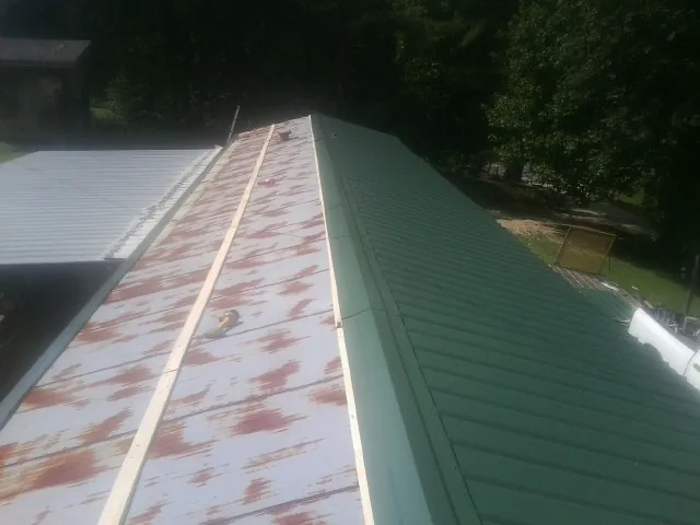 Old rusted panels beside newly installed green metal roofing — Wind Damage Roof Repair by Roofing Brothers in Newton Grove