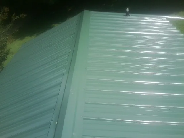New green metal panels meeting at the ridge of a roof — Flat Roof Repair work by our crew in Newton Grove