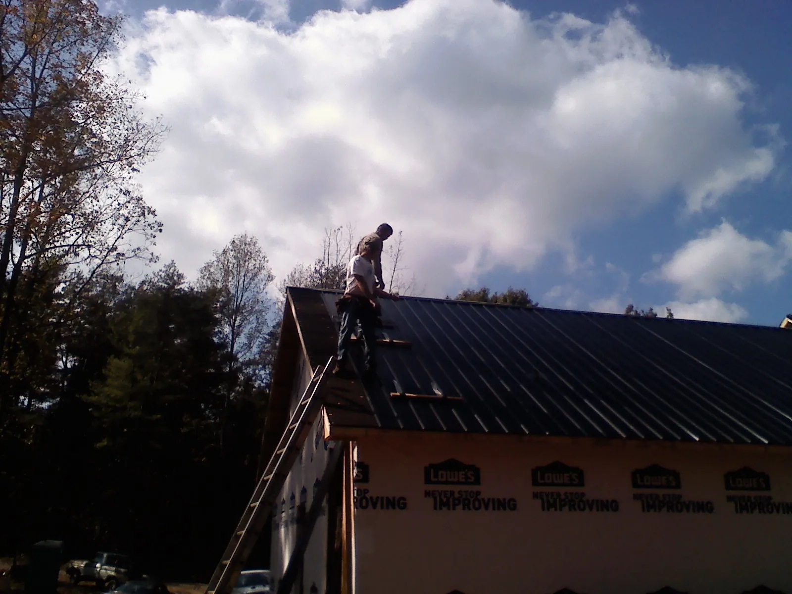 Roofer fastening dark metal panels high against a cloudy sky, from a Roof Inspection job in Newton Grove