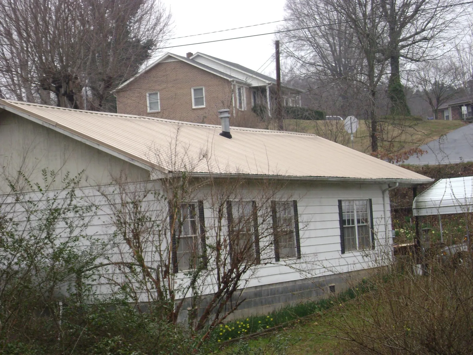 Tan metal roof on a white sided house set into a hillside — Commercial Roofing by Roofing Brothers in Newton Grove