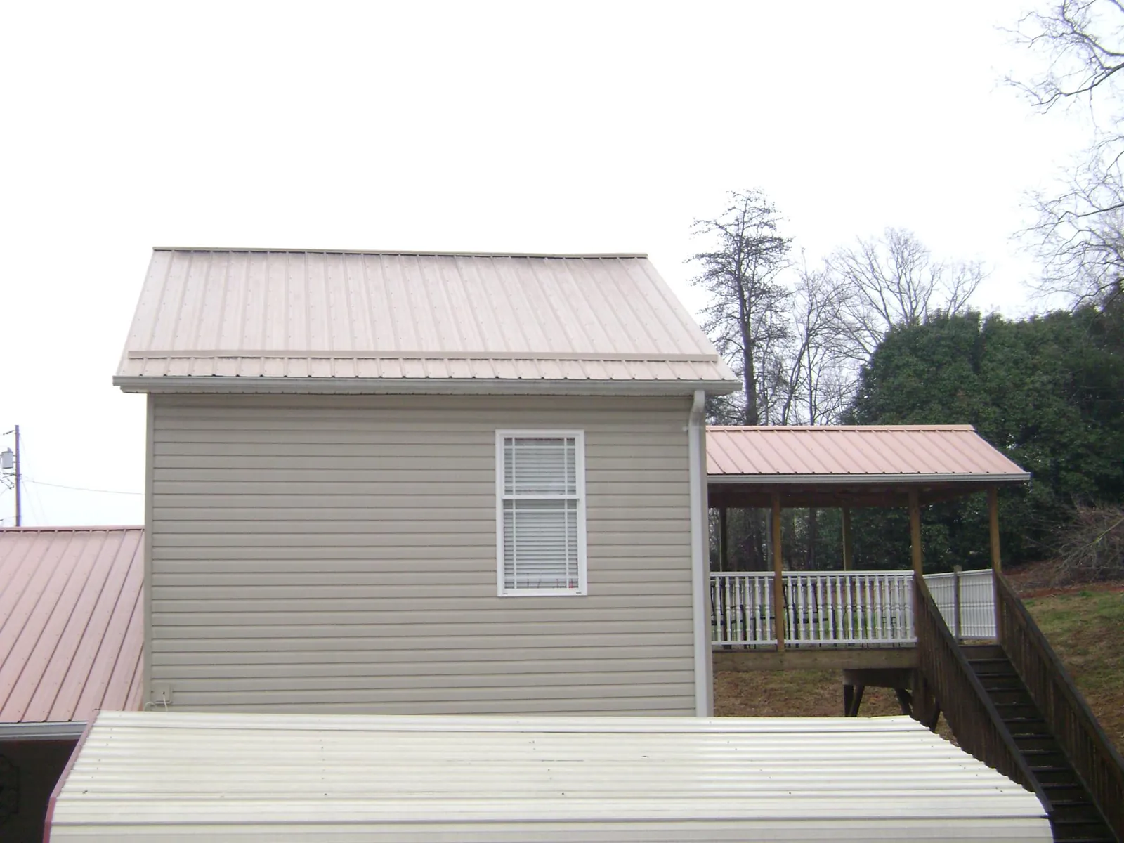 Tan metal roofs on a two story addition and attached porch, from a Roof Replacement job in Newton Grove